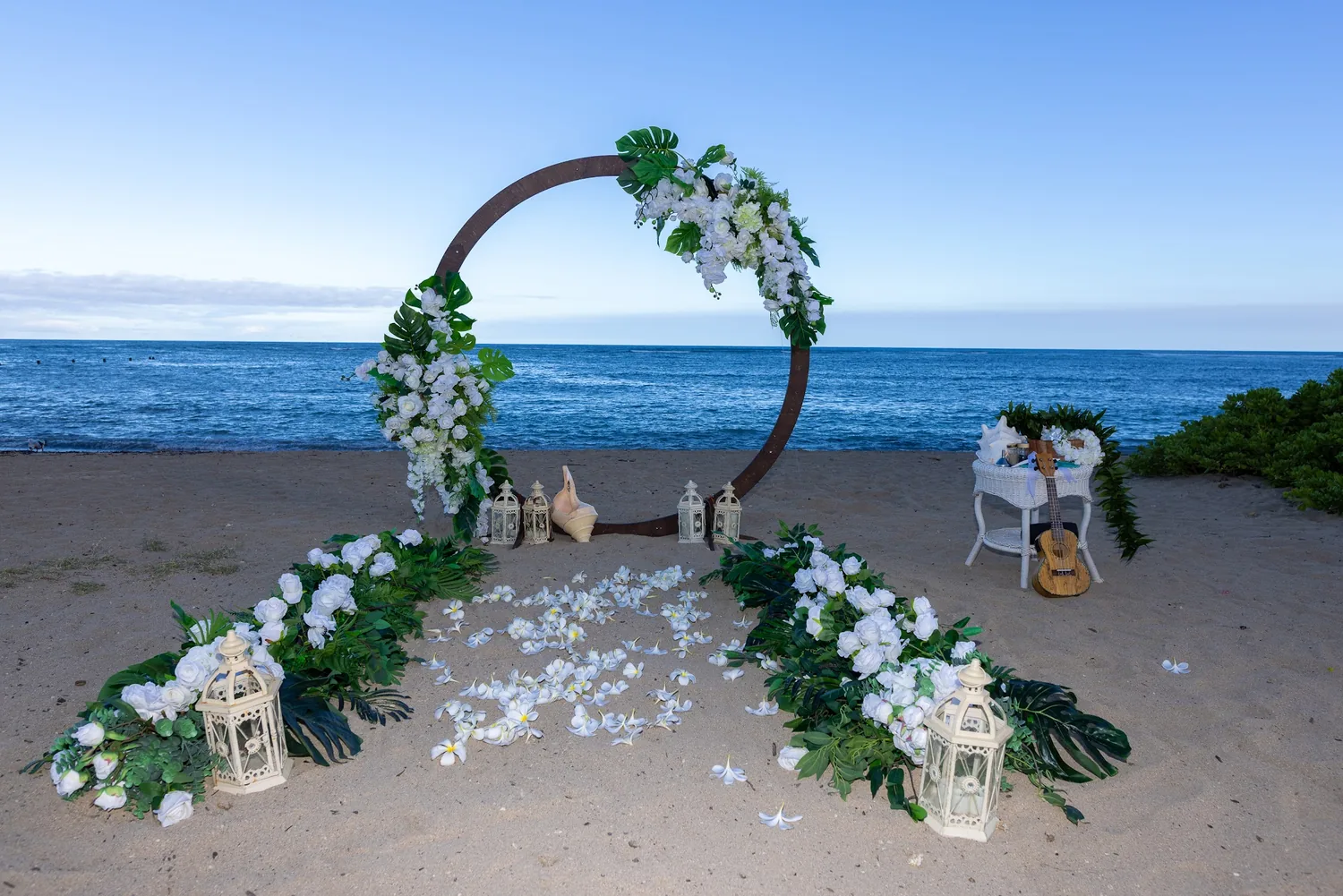 A round archway of white flowers and greenery on the sand at Waialae Beach