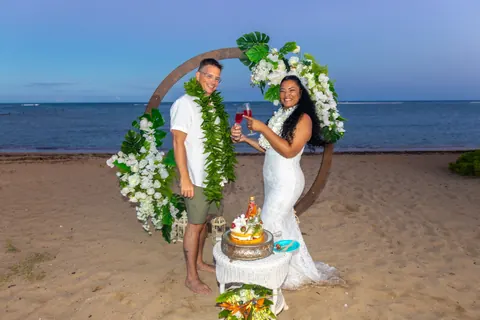The couple with the cake by the archway at dusk