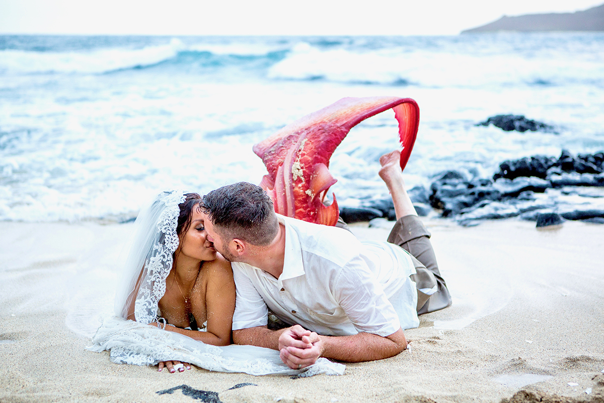 Couple kissing in the surf, the bride in her mermaid gown
