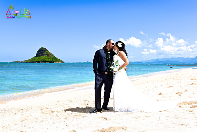 Newlyweds kissing on the green lawn of Kualoa park below the mountains