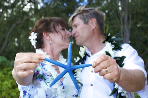 A 25th anniversary couple in leis kissing and holding up a blue starfish in Hawaii