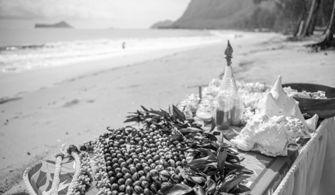 Black and white photo of a wedding table with flower leis on the beach in Hawaii