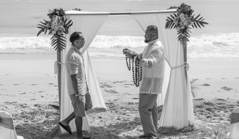 The groom gives his best man a kukui nut and ti leaf lei on the beach on Oahu