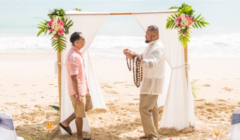 A groom gives his bride a flower lei under the arch at a Hawaii beach wedding