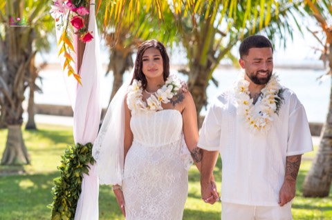 Bride and groom holding hands in white plumeria leis at Magic Island on Oahu
