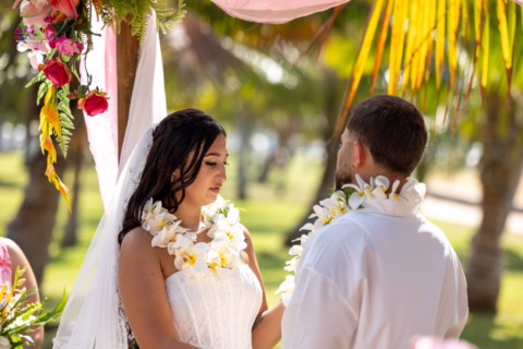 Bride and groom in white plumeria leis facing each other at Magic Island