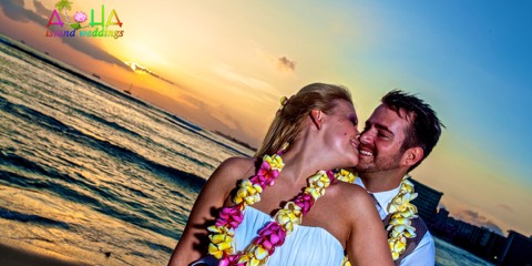 A couple in pink and yellow plumeria leis laughing together at sunset in Waikiki