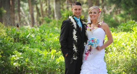 Bride and groom in white leis in a lush green forest on Oahu