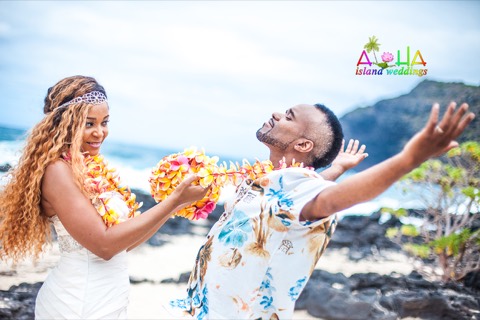 A groom laughs as his bride pulls him close by his flower leis at a Hawaii beach wedding