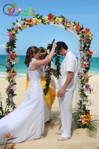 A tea leaf and maile lei for the groom inside a white trellis arch on the beach in Hawaii