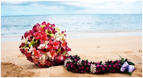 A purple orchid lei with a multi color bouquet on the sand by the sea in Hawaii