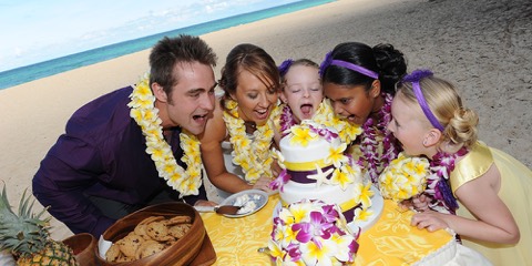 Family and flower girls in leis taking a bite of the wedding cake in Hawaii