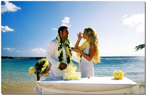 Newlyweds in leis sharing their wedding cake on the beach by the lagoon at Ko Olina