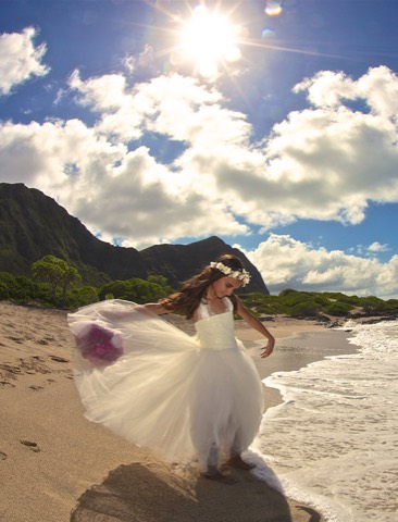 A flower girl twirling in her dress on the beach at Makapuu