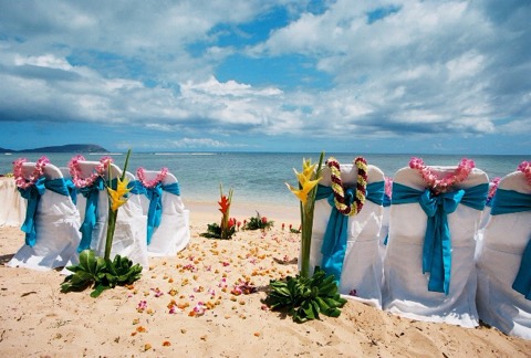 Many different Hawaiian flower leis waiting on the chairs at a beach wedding