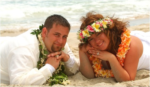 Keith and Anne on the sand wearing light pink and yellow plumeria leis in Hawaii