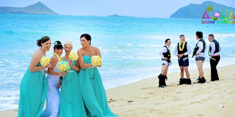 Bridesmaids in turquoise dresses and groomsmen in leis laughing together on the beach on Oahu