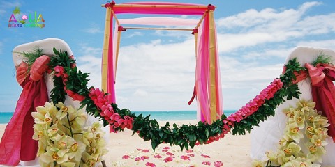 Light green orchid and maile leis wrapped on pink fabric at a beach wedding setup on Oahu