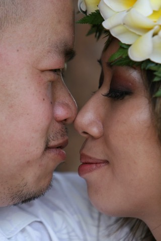A bride in a pink and yellow plumeria lei nose to nose with her groom on Oahu