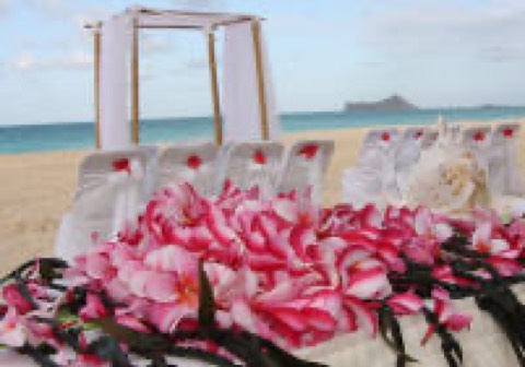 Pink plumeria leis at a beach wedding setup in Hawaii