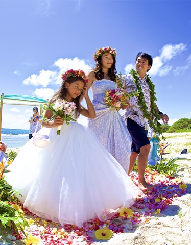 The newlyweds in flower leis walk back down a petal aisle with the flower girl on Oahu