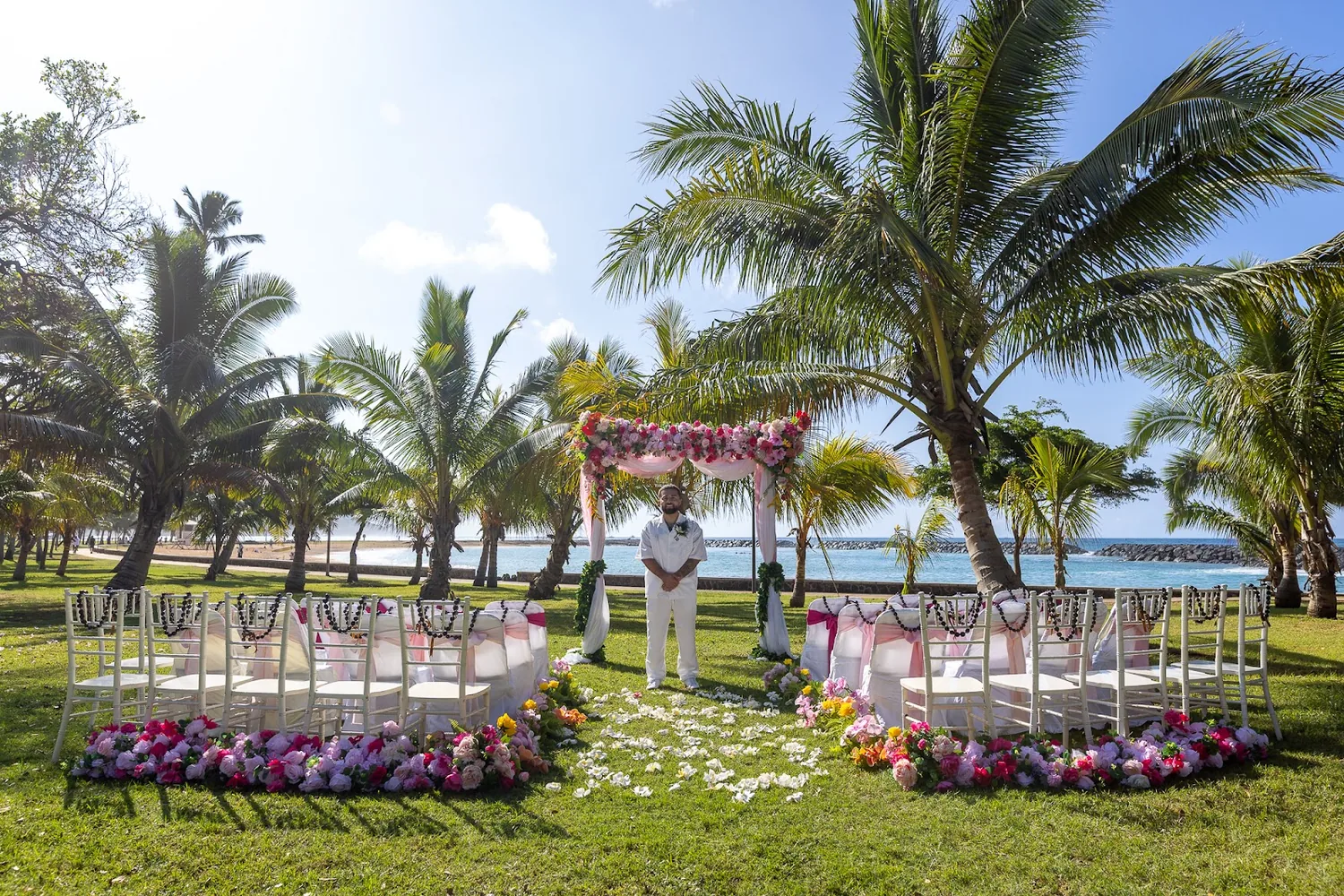 Pink and white wedding arch under the palm trees at Magic Island with chairs and flower aisles