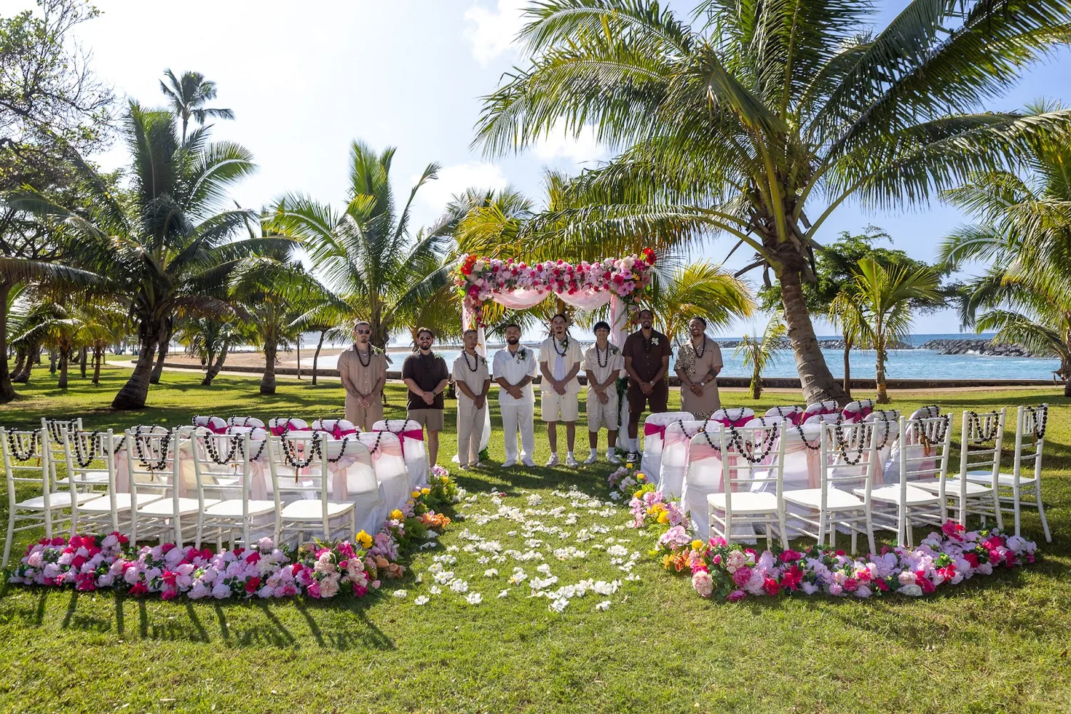The ceremony setup on the grass at Magic Island with pink sashes and petal lined aisles