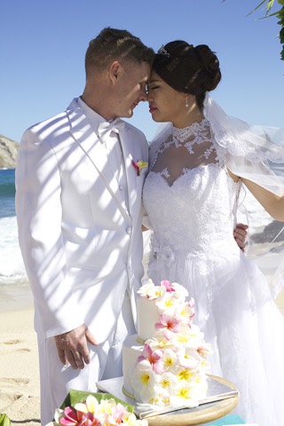 Newlyweds ready to cut their cake after their vows on the beach at Makapuu