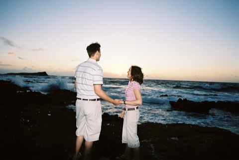Karen and James hold hands on the lava rocks at sunrise