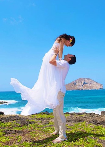 The groom lifts his bride into the air with Rabbit Island behind them