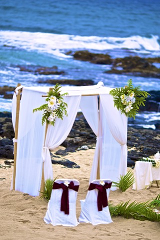 A white wedding arch draped with greenery at Makapuu beach