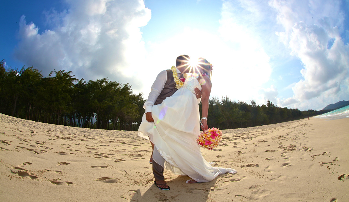 The sun shining through a couple's kiss on the beach after their ceremony