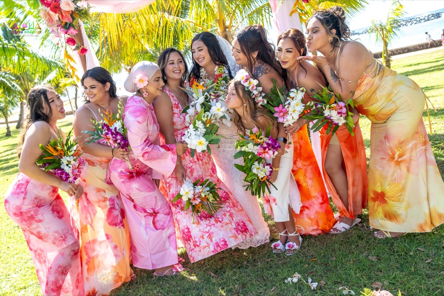 Bridesmaids in pink and orange floral dresses holding tropical bouquets on the lawn