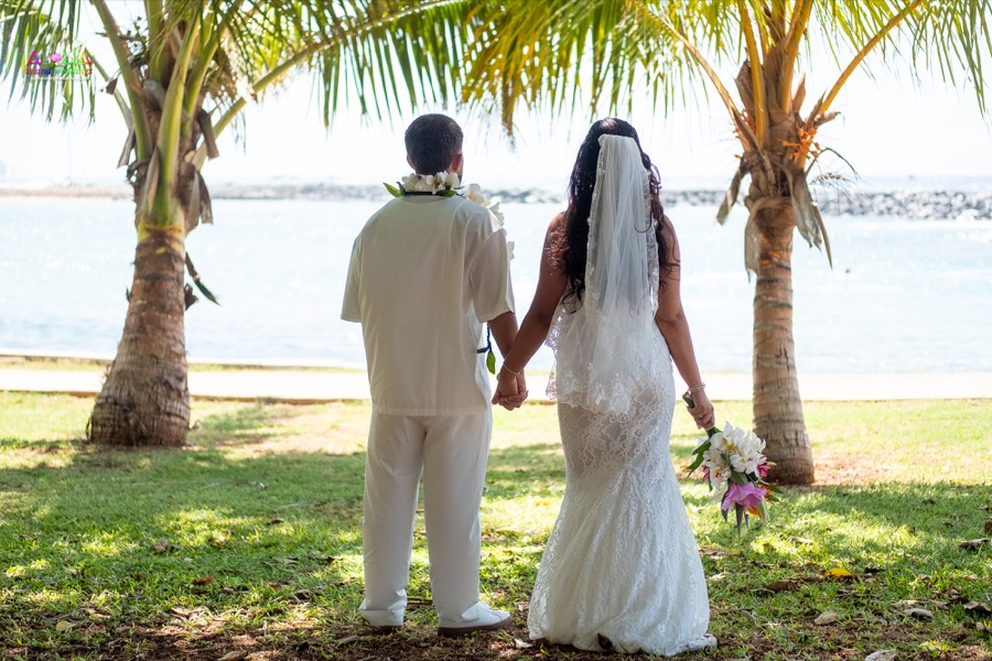 Bride and groom holding hands and looking out at the ocean under the palm trees