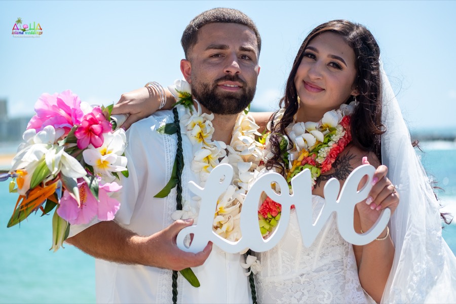 Couple holding up a white wooden love sign by the ocean
