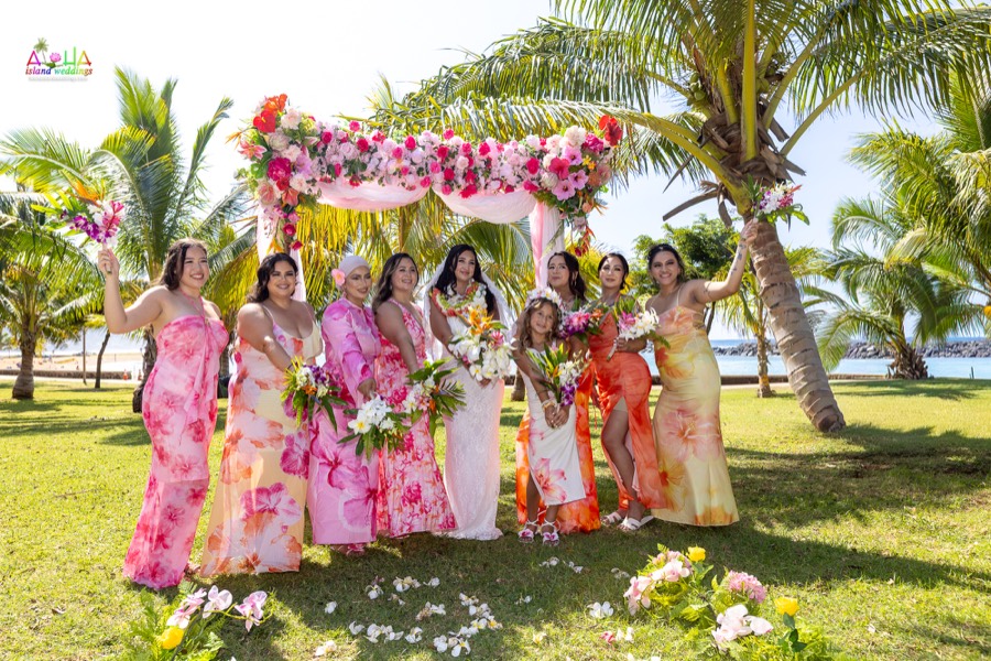 Bride and bridesmaids in colorful floral dresses celebrating by the flower arch