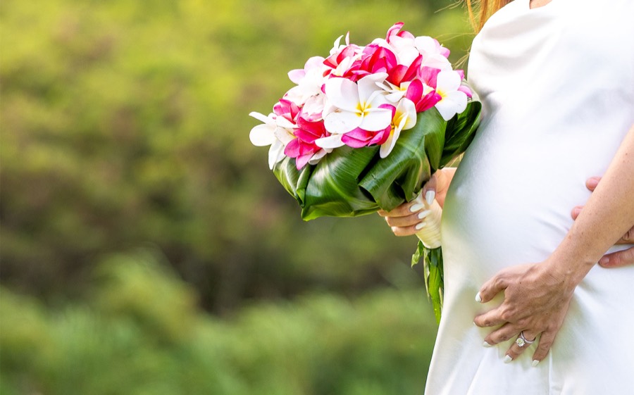 Bride holding a pink and white plumeria bouquet wrapped in ti leaves