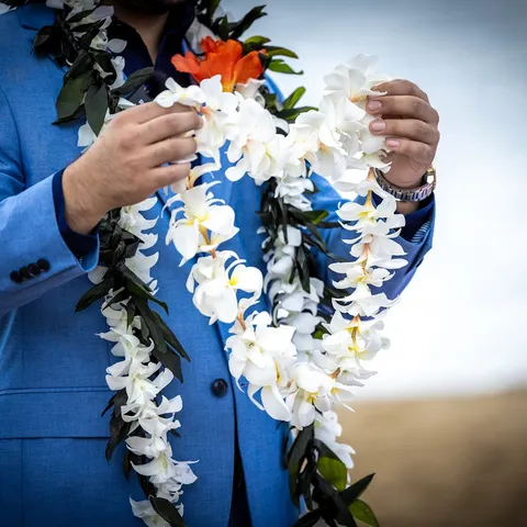 Groom in a blue suit holding white flower leis