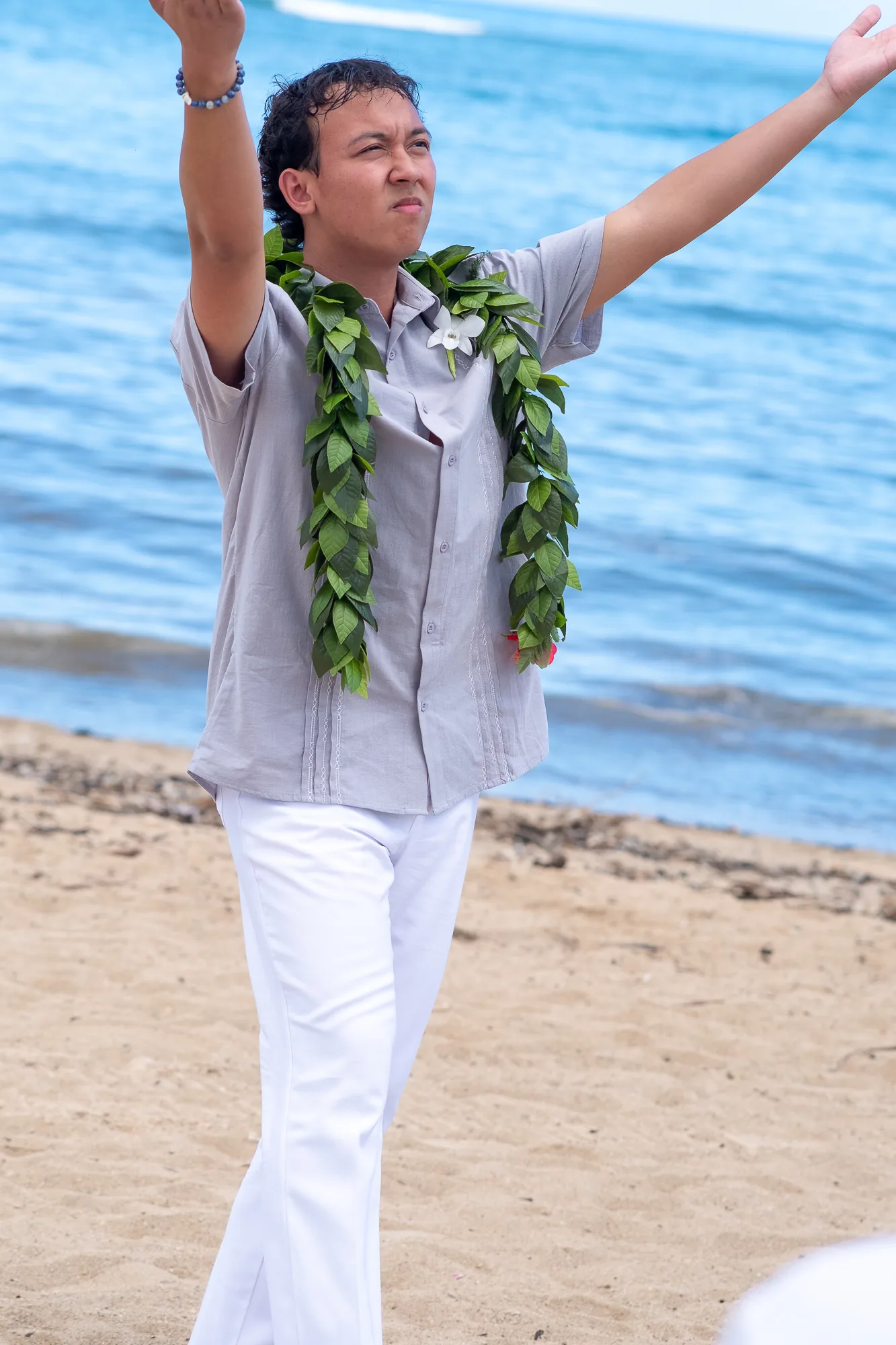 Their son dancing hula with his arms raised by the ocean