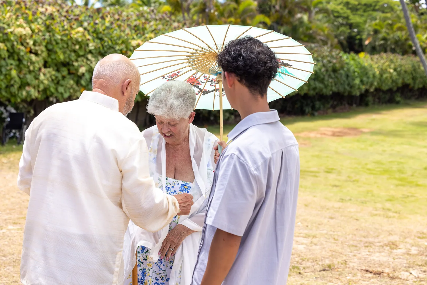 Their parents with a white parasol and their grandson on the lawn