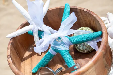 Their rings tied with teal ribbon to starfish in a wooden bowl