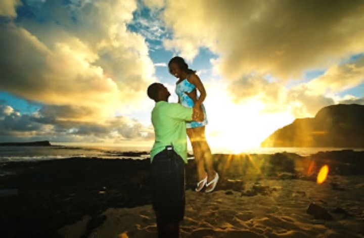 A groom lifting his bride against a golden sunrise at Makapuu Beach Park