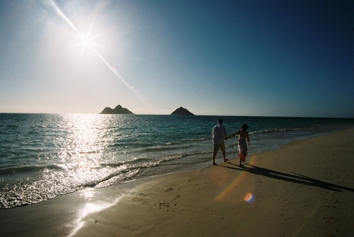 A couple walking along the shore with morning sun sparkling on the water