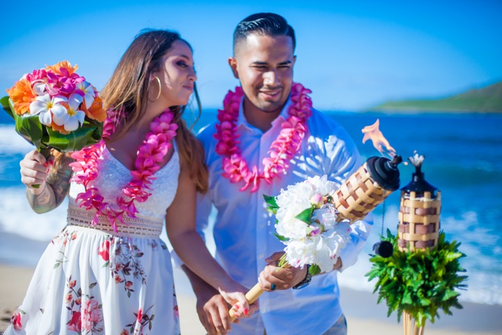 Couple in leis beside flower-topped tiki torches at Makapuu beach
