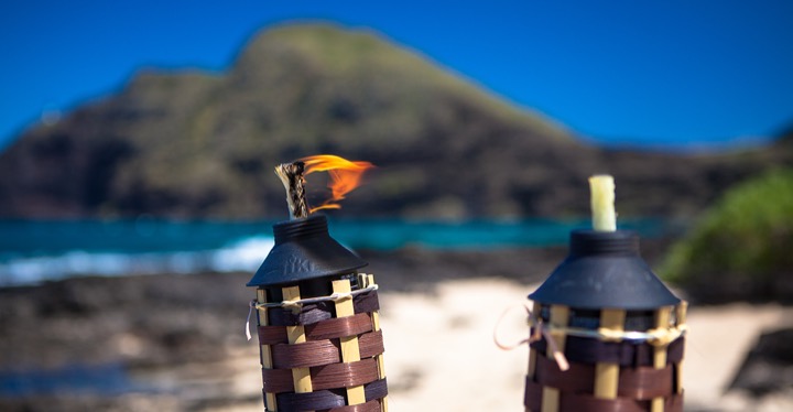 One tiki torch lit and waiting for the couple, with Hawaiian mountains behind