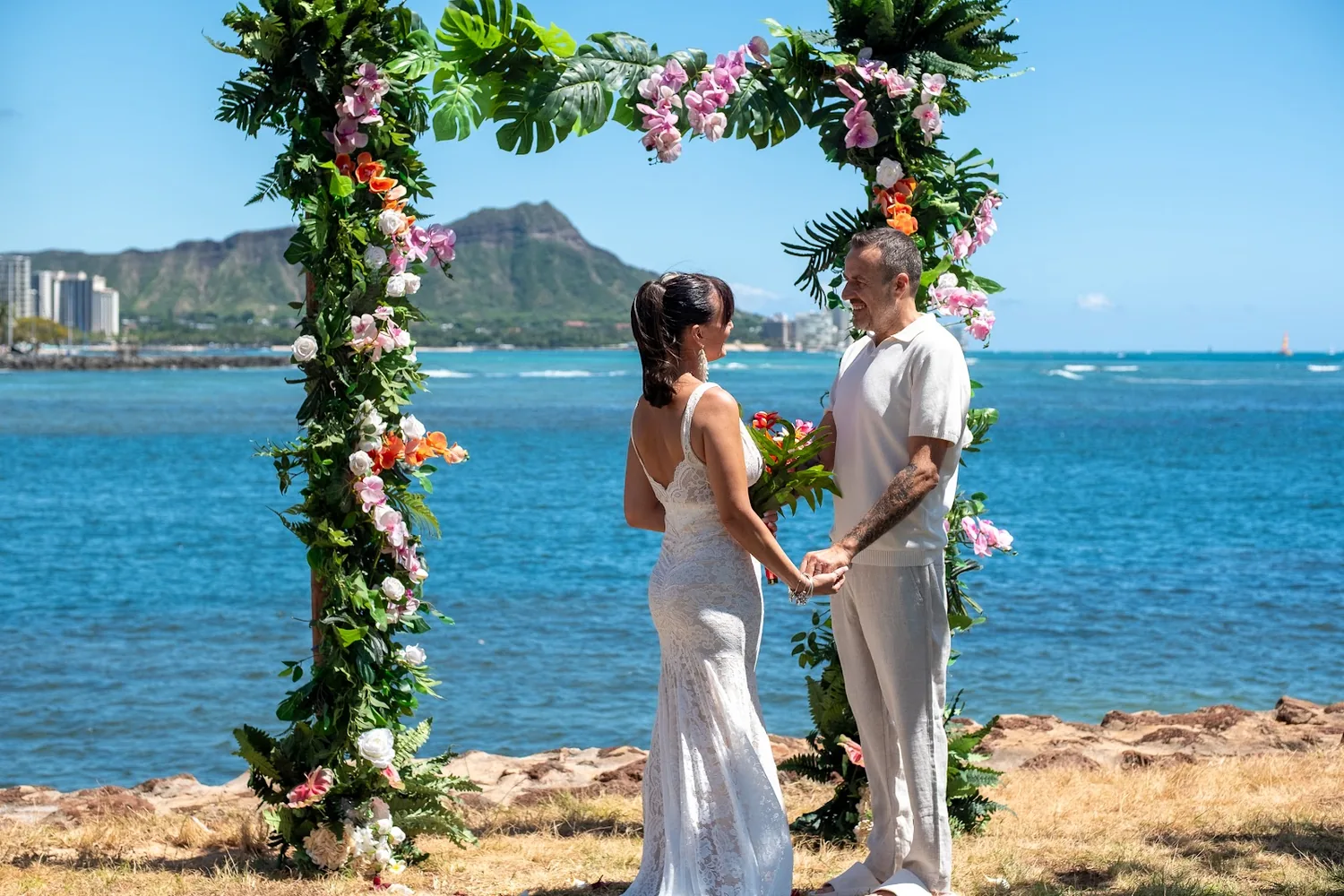 A garden arch of greenery and tropical flowers by the water with Diamond Head behind