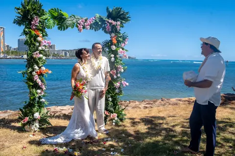 The couple and the officiant at the arch beside the sea