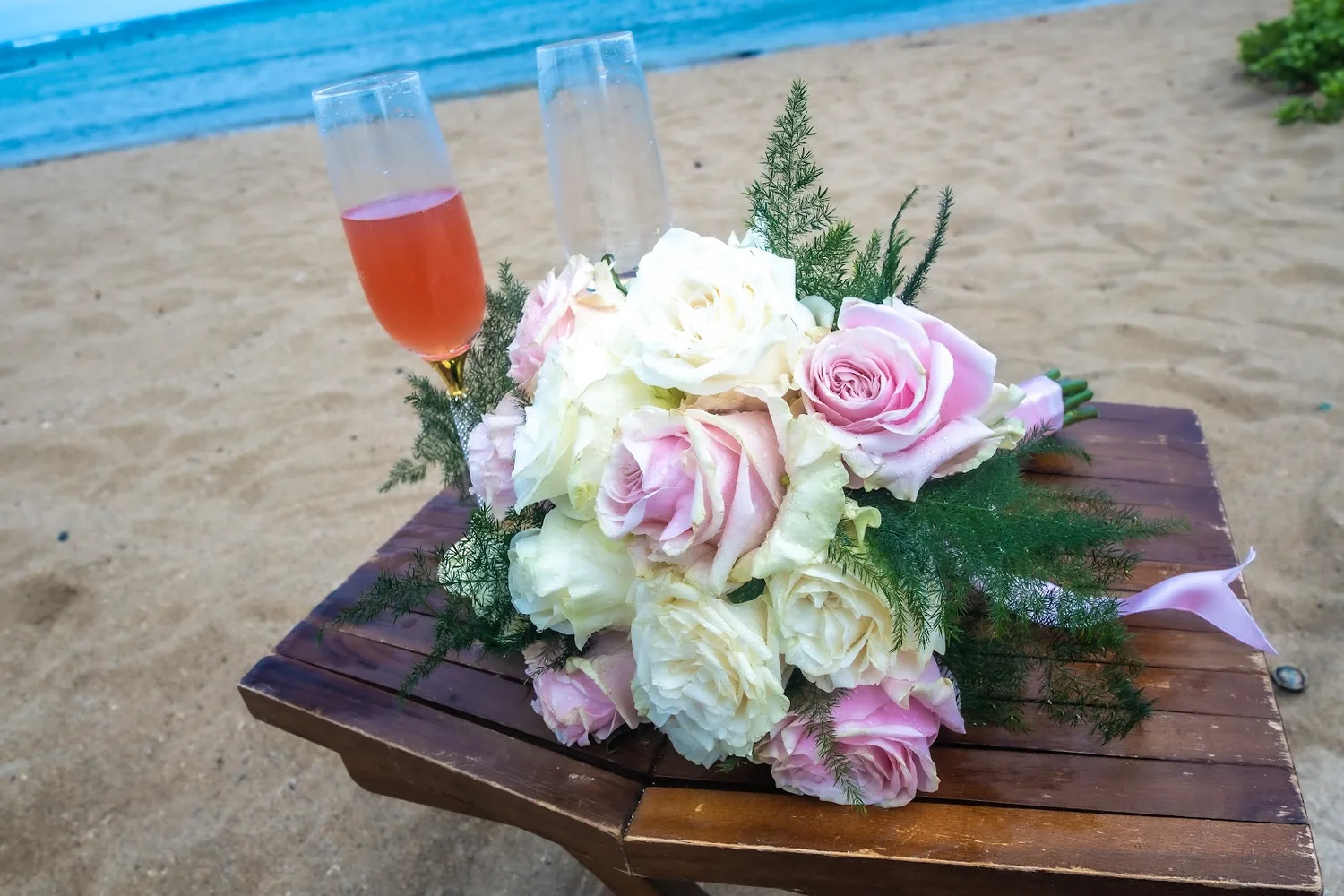 A white and pink bouquet beside two pink drinks on a wooden table