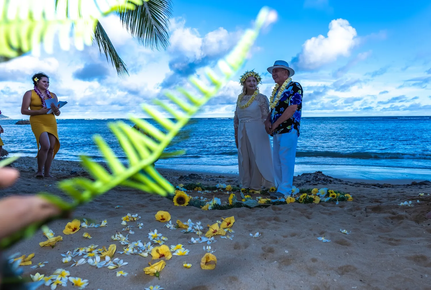 A tropical leaf and yellow flowers framing the ceremony on the sand