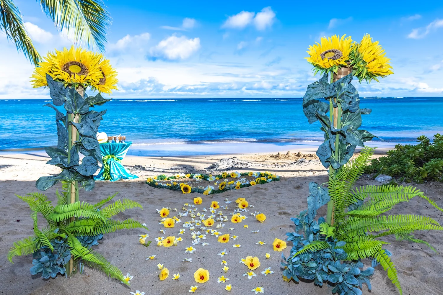 Tall sunflowers and yellow plumeria petals on the sand by the sea